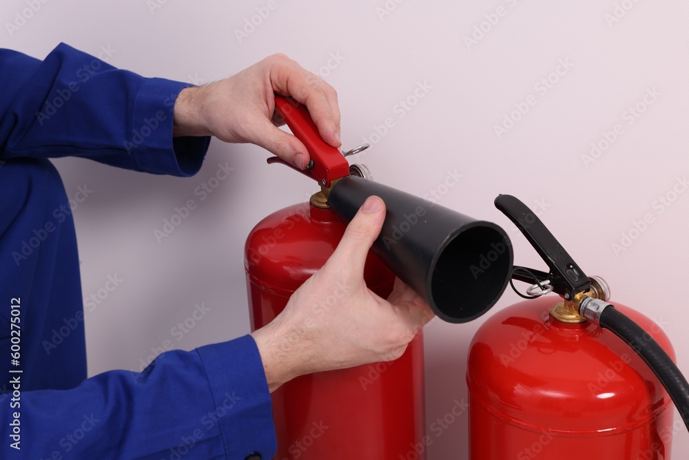Naklejka premium Man checking quality of fire extinguishers indoors, closeup
