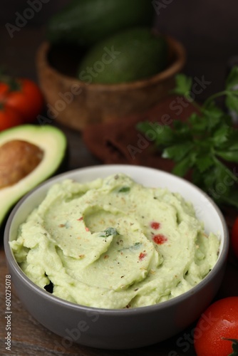 Bowl of delicious guacamole and ingredients on wooden table, closeup