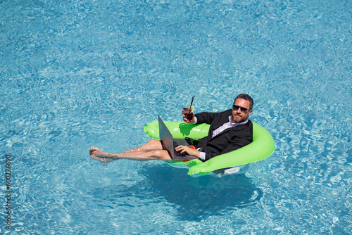 Crazy summer business. Fun business lifestyle. Funny crazy business man in suit using laptop in pool water. Fun businessman. Freelance concept, crazy summer travel. Business success. © Volodymyr