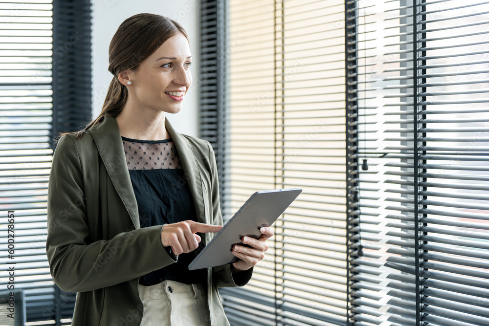 White businesswoman with digital tablet in her hand standing in modern office, smiling and looking away out side. White businesswoman with digital tablet in her hand standing in modern office, smiling and looking away out side.