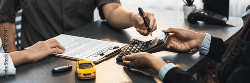 Tela Car dealer calculate interest rate and costs of car loan with calculator, explaining details to customer on term and agreement in dealership office, offering financial and insurance service