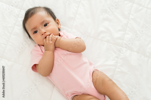 Fotografija infant baby putting hands in mouth and sucking fingers on bed