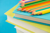 Colorful wooden pencils on a pile of books against light blue background.