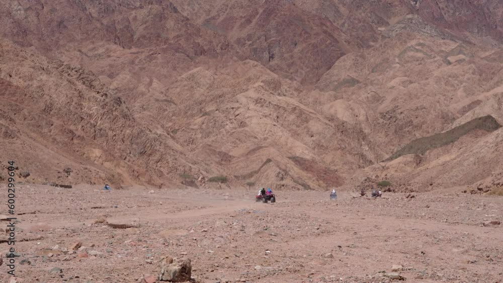 Tourists Riding An ATV Quad Bike In The Rocky Desert. - wide Tourists Riding An ATV Quad Bike In The Rocky Desert. - wide