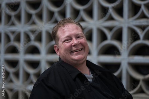 Posing in front of a cinder block wall, a man expresses confidence, joy, and pride in his identity as a disabled trans man living in the city. photo