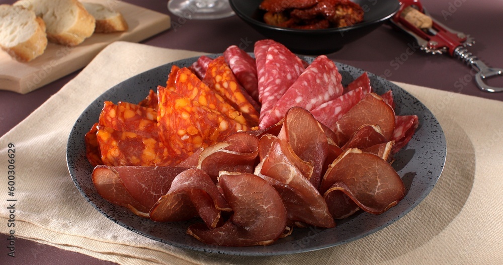 meat slices on a plate. traditional spanish sausage with beef jerky. salchichon, chorizo and prosciutto with glass of wine. serving cold cuts with dried tomatoes and bread. antipasto in sunlight. meat slices on a plate. traditional spanish sausage with beef jerky. salchichon, chorizo and prosciutto with glass of wine. serving cold cuts with dried tomatoes and bread. antipasto in sunlight.
