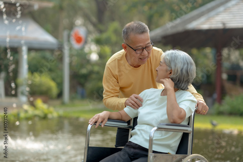 Asian old man caring for his wife in a wheelchair. Elderly couple. Asian couple giving love to each other smiling happily. Happy Asian senior couple in the park