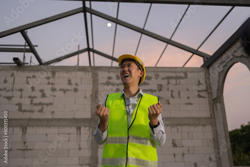 Asian engineer in uniform and helmet at construction site being happy and smiling for success. Successful project and happiness expression after work concept