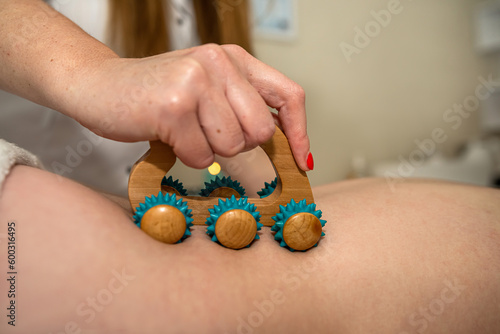 young woman lying on spa and receive anti-cellulite massage on back with wooden roller massager photo