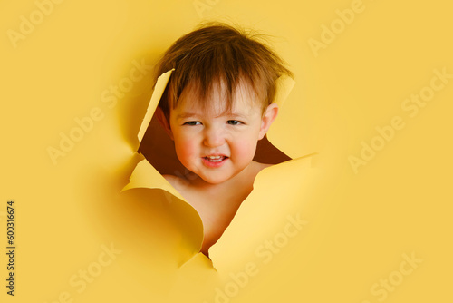 Slika na platnu Happy baby in a hole on a paper yellow background