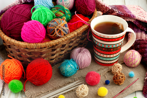 Lots of balls of yarn and a cup of tea. Handicraft in a cozy environment. Knitting from colorful yarn in a basket.