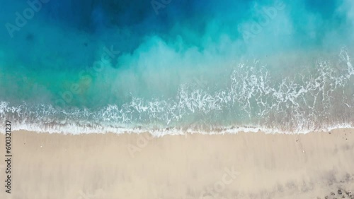 Aerial top view of beautiful footage while turquoise sea waves breaking on beach sandy coastline. Aerial top shot of golden beach with ocean blue emerald water and white foam waves. Relaxing footage.