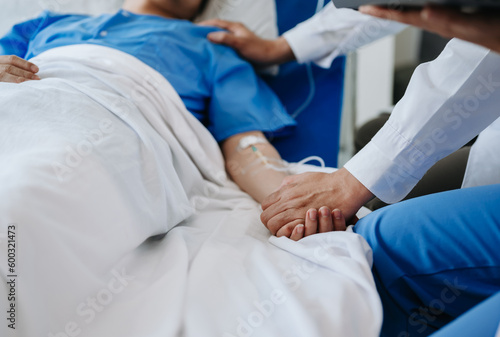 Female doctor holding male patient hand on the bed with receiving saline solution in hospital .