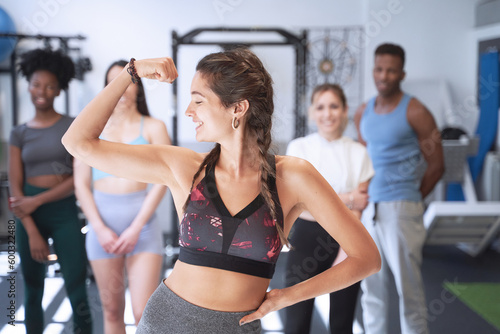 Woman showing her arm muscle while posing in front of a group of people at the gym. Sports concept.