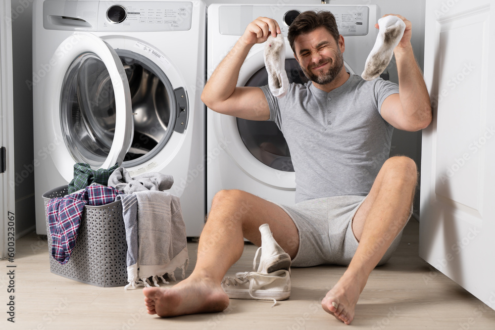 Confused man setting washing laundry machine. Male struggling and  frustrating while doing housework and daily routine at home, Stock image