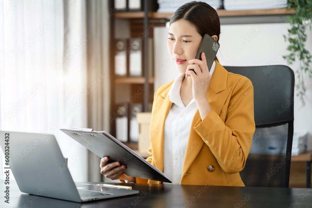 Young Asian businesswoman involved in cellphone call conversation working on computer, giving professional consultation to client or negotiating project. Young Asian businesswoman involved in cellphone call conversation working on computer, giving professional consultation to client or negotiating project.