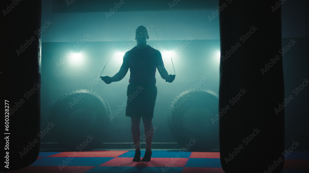 Fototapeta premium Fighter does some jump rope exercises in dark room under light
