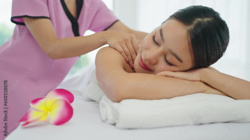 Close up face of beautiful young Asian woman lying on massage bed getting relaxing. Therapist massaging to shoulders of woman lying on massage bed at spa salon Close up face of beautiful young Asian woman lying on massage bed getting relaxing. Therapist massaging to shoulders of woman lying on massage bed at spa salon