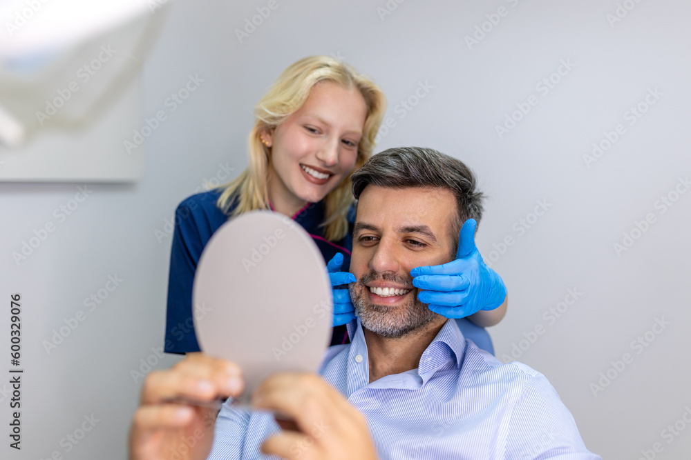 Fototapeta premium Handsome man smiling while looking at mirror in dental clinic. Shot of a Male patient checking her results in the dentists office