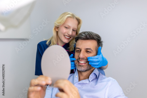 Handsome man smiling while looking at mirror in dental clinic. Shot of a Male patient checking her results in the dentists office