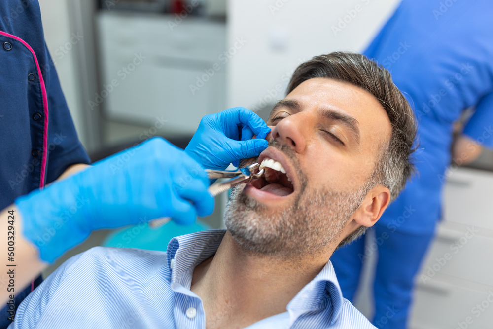 Treatment of a patient with a dentist surgeon. Extraction of teeth and prosthetics. Doctor performing extraction procedure with forceps removing patient tooth. Healthcare dentistry medicine concept Treatment of a patient with a dentist surgeon. Extraction of teeth and prosthetics. Doctor performing extraction procedure with forceps removing patient tooth. Healthcare dentistry medicine concept