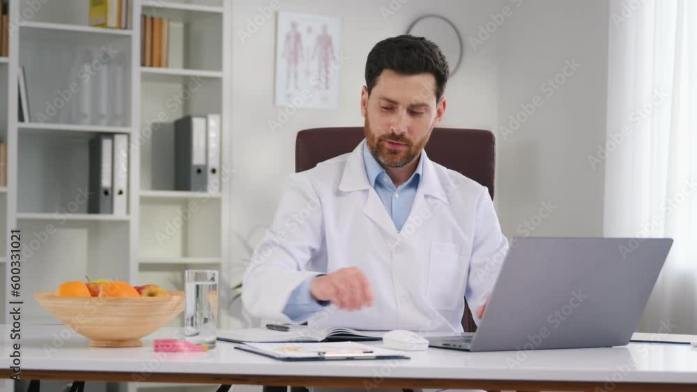 Writing data into the document. By the table with laptop. Doctor in formal clothes is working in the cabinet. Writing data into the document. By the table with laptop. Doctor in formal clothes is working in the cabinet.