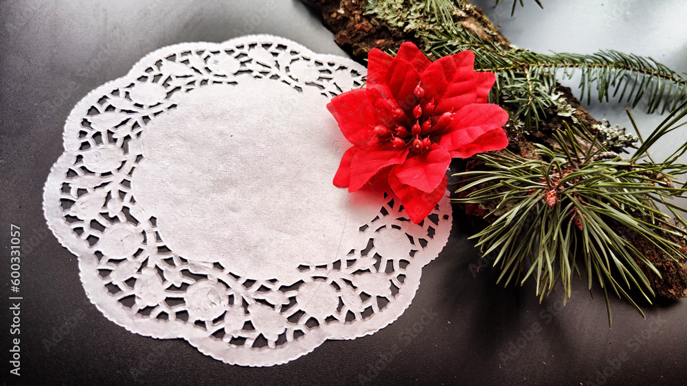 Fototapeta premium Black frame, white round napkin, green pine branch, red flower on background with reflections and sparkle of light. Abstract location for photo shoot. Cchristmas table decor. Concept of winter holiday