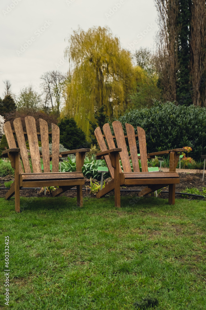 Two Wooden lounges chairs placed on spacious terrace of modern country house surrounded with green plants garden furniture outdoor for relaxing on summer days. Garden landscape with two chairs in