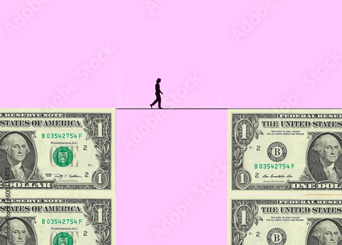 Silhouette of woman walking tightrope between two blocks made of one dollar bills photo
