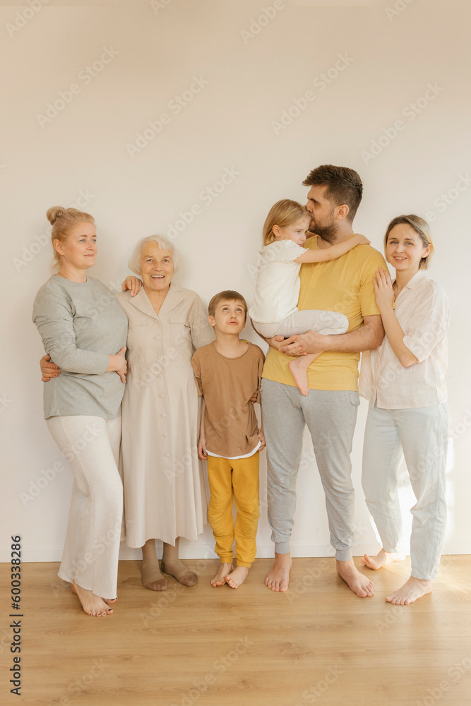 Happy multi-generation family standing together in front of wall at home Happy multi-generation family standing together in front of wall at home