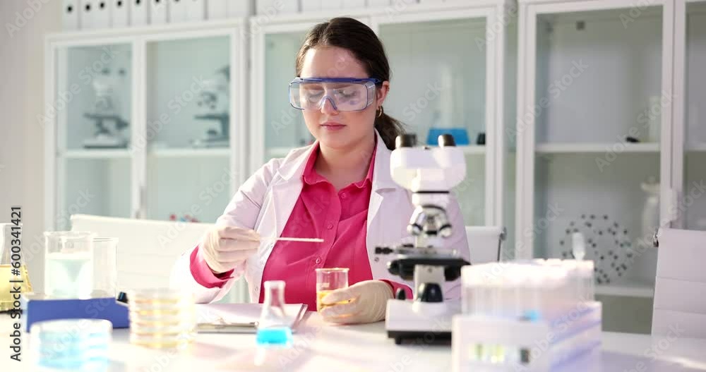 Laboratory assistant checks results of patient urine test. Specialist in gloves sits at table and examines sample of yellow liquid Laboratory assistant checks results of patient urine test. Specialist in gloves sits at table and examines sample of yellow liquid