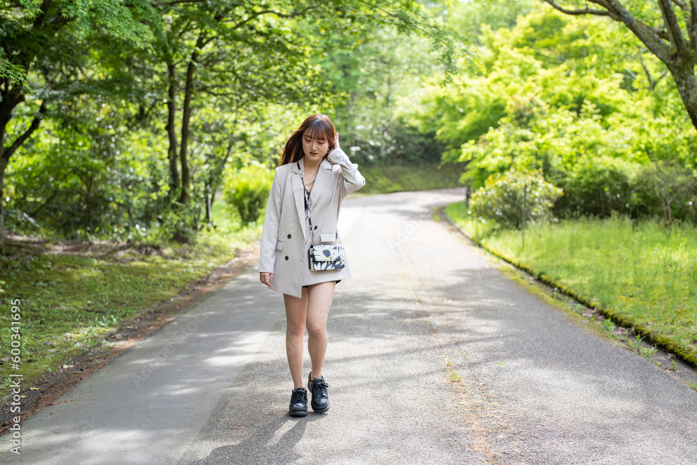 A young Japanese woman in her twenties, wearing a white jacket and shorts, walking through a forest in a large nature park in Hakui City, Ishikawa Prefecture. A young Japanese woman in her twenties, wearing a white jacket and shorts, walking through a forest in a large nature park in Hakui City, Ishikawa Prefecture.