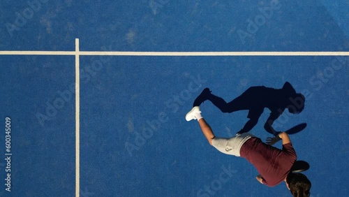 Overhead top view shots of a young handsome padel player hitting the ball with a smash bandeja vibora on the fly.

