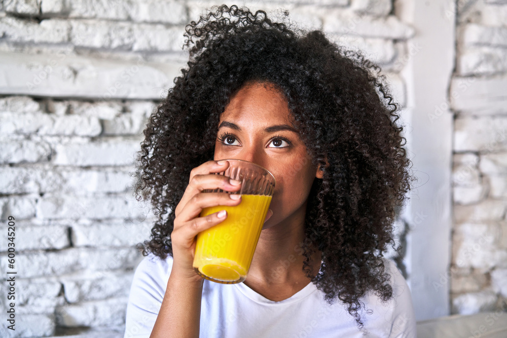 African-American woman enjoys freshly squeezed orange juice on sofa, morning light. - obrazy, fototapety, plakaty 