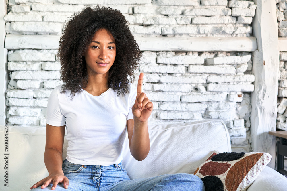 A young african american woman sitting on her sofa showing number one with finger. A young african american woman sitting on her sofa showing number one with finger.