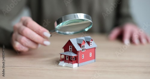 Appraiser is holding magnifying glass and examining miniature of house. Home appraisal and sale photo