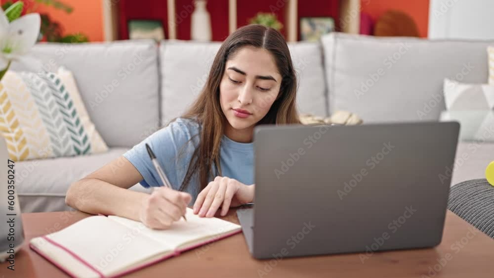 Young beautiful hispanic woman using laptop taking notes at home Young beautiful hispanic woman using laptop taking notes at home