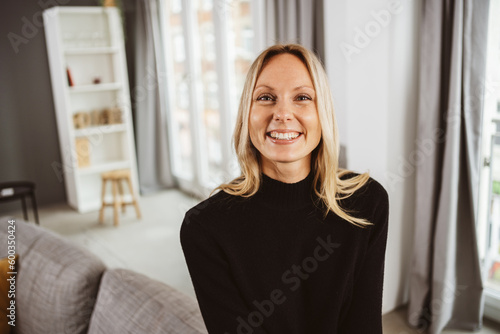 Laughing young blonde woman sitting on the sofa and looking at the camera
