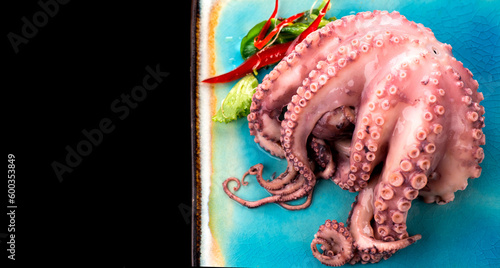 Octopus serving with vegetables, sea food. Freshly boiled octopus on a blue plate, Mediterranean cuisine, dinner. Border design on black background