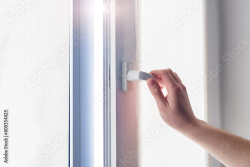 A man's hand holds a plastic window handle.Manual opening white plastic pvc window at home.A man opens a window, closes a plastic frame in his apartment. Roller Blinds. 