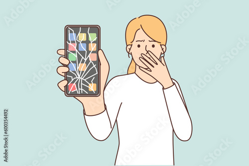 Woman with broken phone covers mouth with hand and demonstrates screen of gadget with cracks