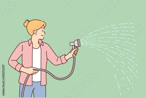 Woman with hose waters lawn with grass tending to sward in backyard to avoid drying out plants