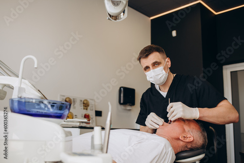 Male dentist using dental drill while working on mature patient s teeth.