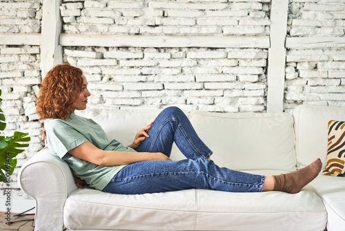 Relaxed young redhead woman lounging on her sofa at home, with a content smile.