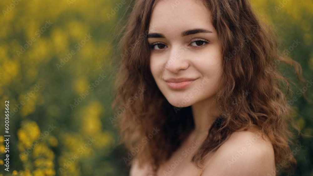 Happy girl in spring yellow rapeseed posing in front of the camera and smiling sincerely. Portrait of a beautiful young woman with curly hair Happy girl in spring yellow rapeseed posing in front of the camera and smiling sincerely. Portrait of a beautiful young woman with curly hair