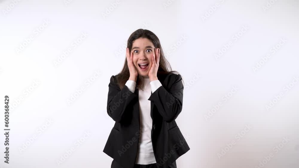 Smartly dressed young professional lady with dark hair rising her arms and drawing her palms to her cheeks while looking pleasantly surprised Smartly dressed young professional lady with dark hair rising her arms and drawing her palms to her cheeks while looking pleasantly surprised