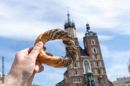 Hand holding obwarzanek krakowski pretzel on Cracow Main Market Square. St. Mary's Basilica, Bazylika Mariacka Kraków or Kościół Mariacki Church in bg. Krakowskie obwarzanki food in Krakow, Poland.