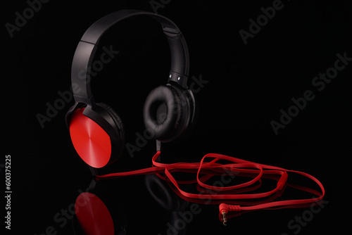 Black headphones with red inserts and a red wire on a black background,