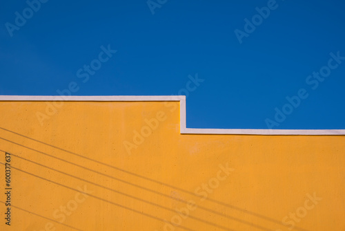 Minimal Exterior Architecture Background of yellow Building Wall with shadow of electric cable lines on surface against blue clear sky