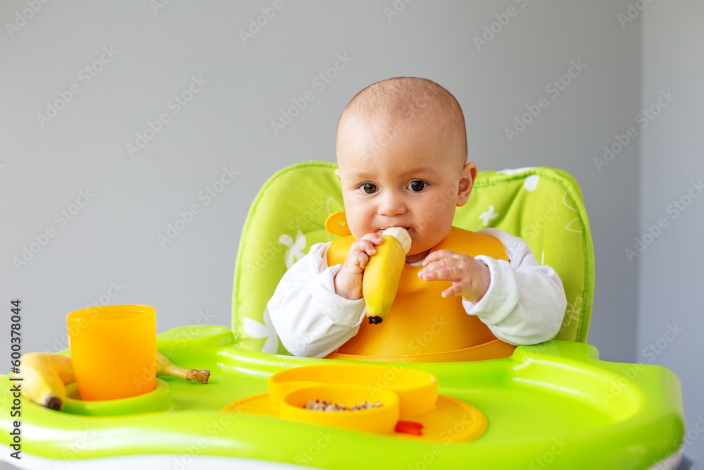 Baby girl eats quinoa porridge and banana while sitting on high chair. Baby feeding concept. Baby girl eats quinoa porridge and banana while sitting on high chair. Baby feeding concept.